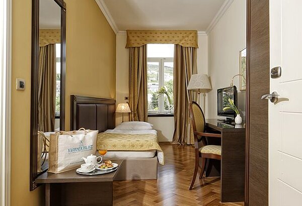 Ein gemütliches Hotelzimmer mit einem Einzelbett, einem Tisch und einem Stuhl. Auf dem Tisch stehen ein Frühstückstablett mit einer Tasse Kaffee, einem Croissant und einem Glas Saft. Große Fenster ... Historisches Hotel, Kroatien - Ihr Komfort-Einzelzimmer