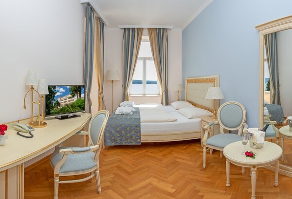 Helles Hotelzimmer mit einem Doppelbett, einem Schreibtisch und einem Fernseher. Ein großer Spiegel und ein kleiner Tisch mit Stühlen sind ebenfalls vorhanden. Die Fenster lassen viel Tageslicht he... Familienfreundliche Suite in Kroatien für Ihren Urlaub