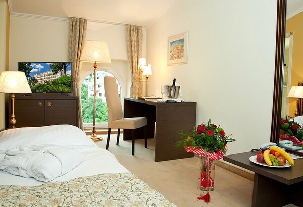 Ein gemütliches Hotelzimmer mit einem Einzelbett, einem Fernseher, einem Schreibtisch und einem Stuhl. Auf dem Tisch stehen eine Flasche Sekt und ein Blumenstrauß. Ein Obstteller ist ebenfalls sich... Einzelzimmer im historischen Hotel in Crikvenica