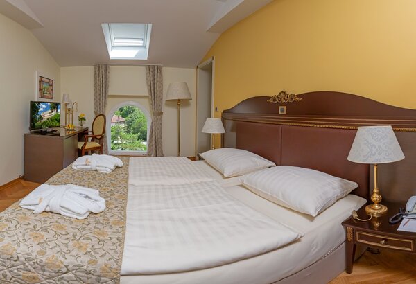 Ein helles Hotelzimmer mit zwei Einzelbetten, einem Fernseher und einem Schreibtisch. Große Fenster bieten Blick auf den Garten. Die Wände sind in sanften Farben gehalten, und die Einrichtung ist e... Kvarner Bucht - Urlaub im Komfort Doppelzimmer